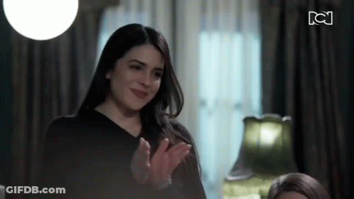 A Woman In A Black Shirt Is Clapping Her Hands In Front Of A Sign That Says Tc GIF