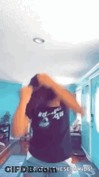 A Woman In A Black Shirt Is Dancing In A Living Room With Her Hands In Her Hair . GIF