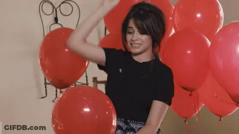 A Woman In A Black Shirt Is Dancing In Front Of A Bunch Of Red Balloons GIF