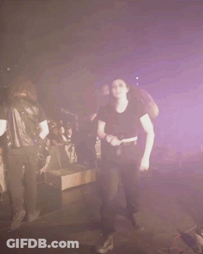 A Woman In A Black Shirt Is Dancing In Front Of A Crowd Of People GIF