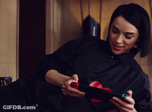 A Woman In A Black Shirt Is Holding A Nintendo Switch In Her Hands GIF