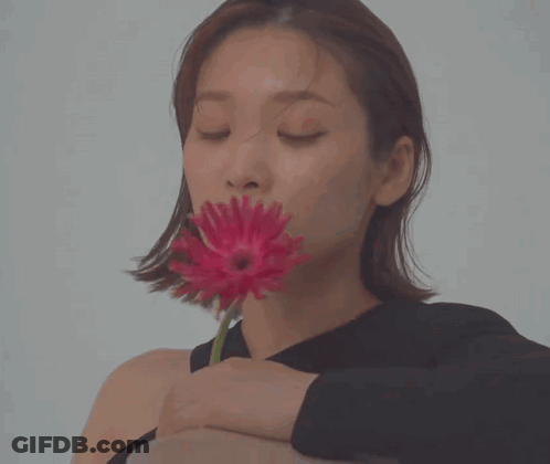 A Woman In A Black Shirt Is Holding A Red Flower In Her Hand GIF