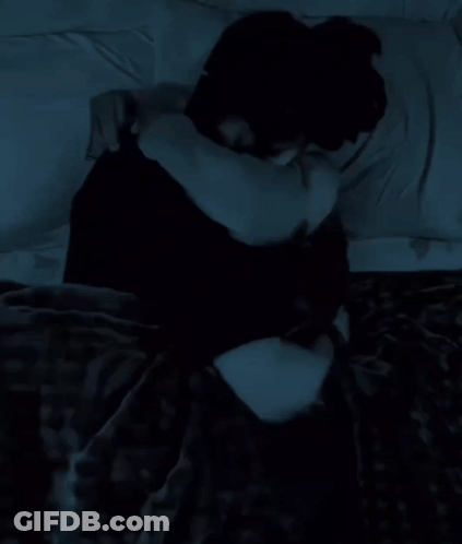 A Woman In A Black Shirt Is Laying On A Bed With A White Pillow GIF