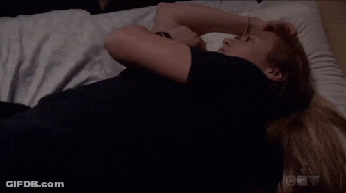 A Woman In A Black Shirt Is Laying On A Bed With Her Arms Crossed . GIF
