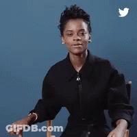 A Woman In A Black Shirt Is Sitting In A Chair With Her Hands Folded . GIF