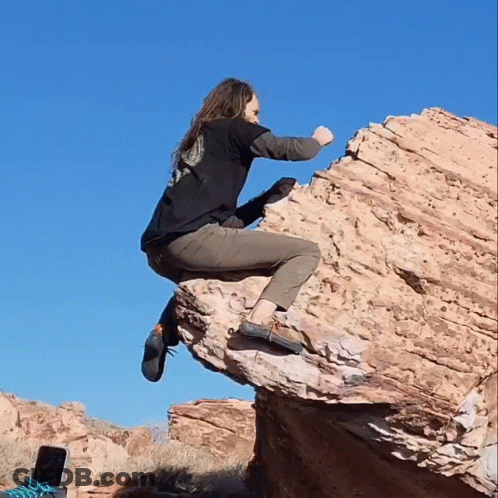 A Woman In A Black Shirt Is Sitting On A Large Rock GIF