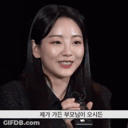 A Woman In A Black Shirt Is Smiling And Holding A Microphone With Korean Writing On The Bottom GIF