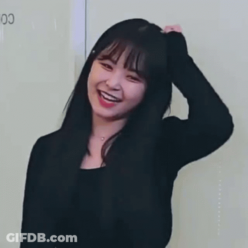 A Woman In A Black Shirt Is Smiling And Touching Her Hair . GIF