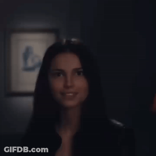 A Woman In A Black Shirt Is Smiling In Front Of A Framed Picture GIF