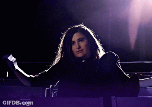 A Woman In A Black Shirt Is Standing In A Dark Room GIF