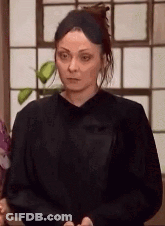A Woman In A Black Shirt Is Standing In Front Of A Window And Looking At The Camera . GIF