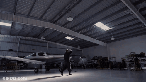 A Woman In A Black Shirt Stands With Her Arms Outstretched In A Dark Room GIF