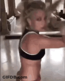 A Woman In A Black Sports Bra Is Standing In A Room With Her Arms Outstretched . GIF