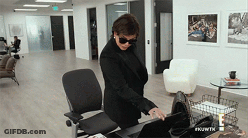 A Woman In A Black Suit And Sunglasses Is Standing At A Desk With A Laptop .. GIF