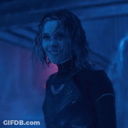 A Woman In A Black Suit Is Smiling In A Dark Room GIF