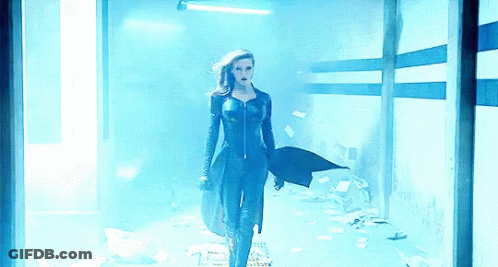 A Woman In A Black Suit Is Standing In A Dark Room GIF