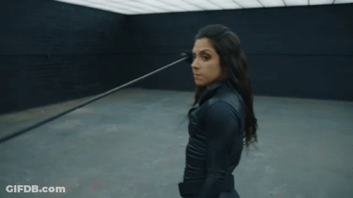 A Woman In A Black Suit Is Standing In A Dark Room With Her Arms Outstretched GIF
