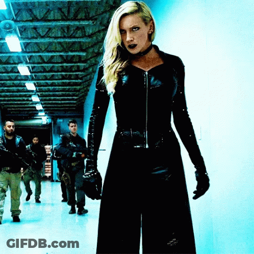 A Woman In A Black Suit Is Standing In A Hallway With A Group Of Men GIF