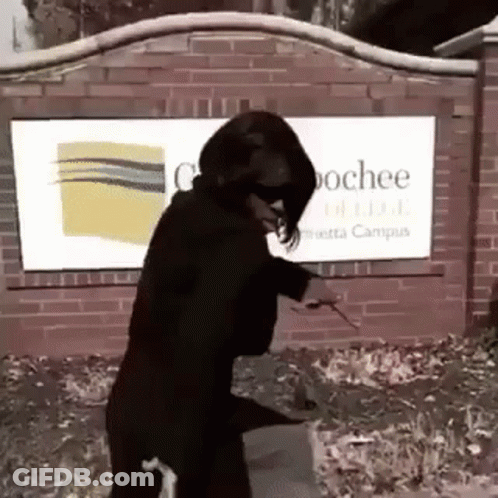 A Woman In A Black Suit Is Standing In Front Of A Brick Wall With A Sign . GIF