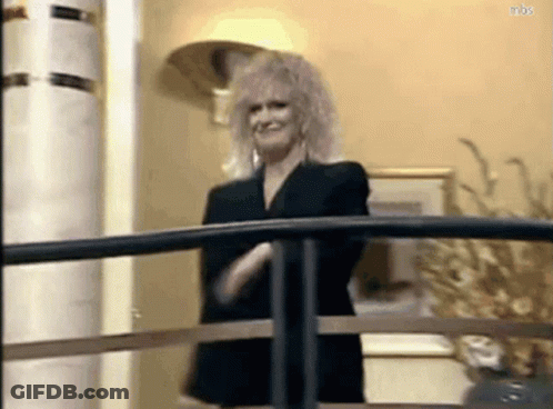 A Woman In A Black Suit Is Standing On A Balcony With Her Arms Crossed . GIF