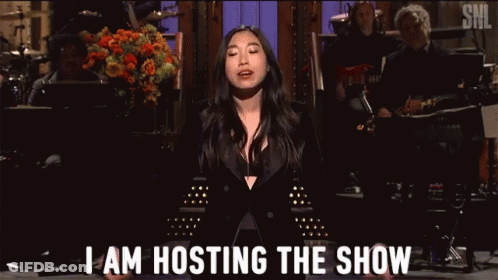 A Woman In A Black Suit Is Standing On A Stage And Says I Am Hosting The Show . GIF