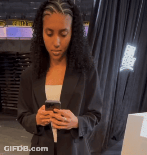 A Woman In A Black Suit Looks At Her Phone GIF
