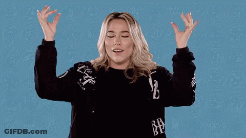 A Woman In A Black Sweater Is Raising Her Arms In The Air GIF