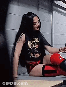 A Woman In A Black Tank Top And Red Shorts Is Sitting On A Bench . GIF