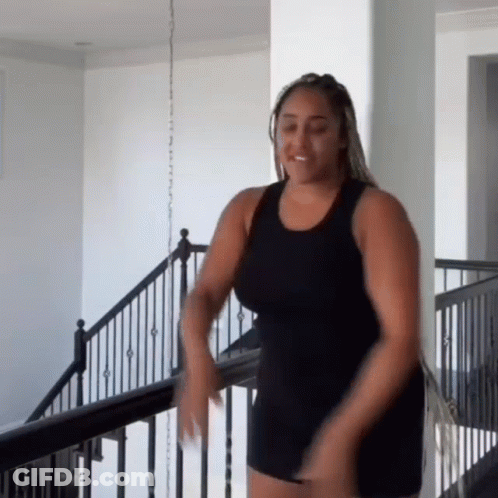 A Woman In A Black Tank Top And Shorts Is Dancing On A Staircase . GIF