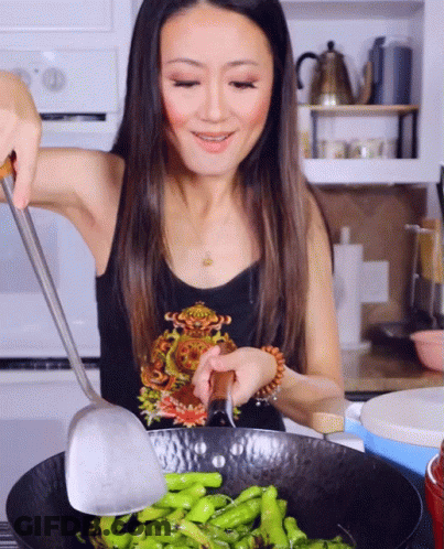 A Woman In A Black Tank Top Is Cooking Green Beans In A Wok GIF