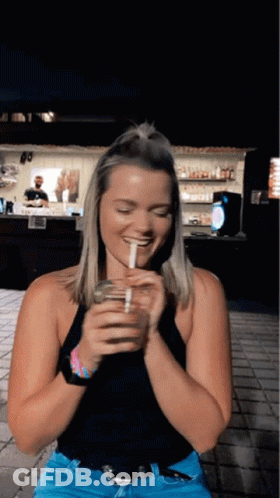 A Woman In A Black Tank Top Is Drinking From A Glass With A Straw GIF