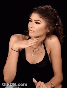 A Woman In A Black Tank Top Is Holding Her Hand To Her Face And Making A Funny Face . GIF