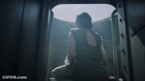 A Woman In A Black Tank Top Is Looking Out A Window GIF