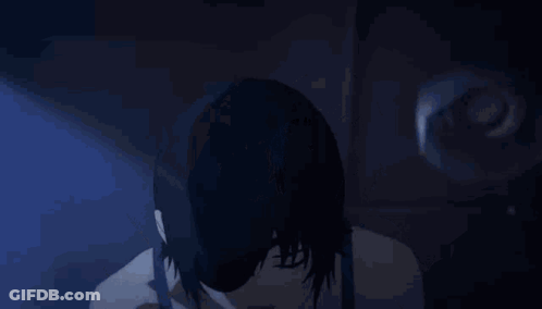 A Woman In A Black Tank Top Is Pointing Up With Her Fingers . GIF