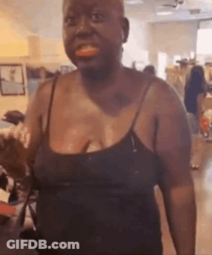 A Woman In A Black Tank Top Is Standing In A Living Room And Smiling . GIF