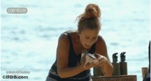 A Woman In A Black Tank Top Is Standing In Front Of A Body Of Water With The Time Of 1:45 GIF