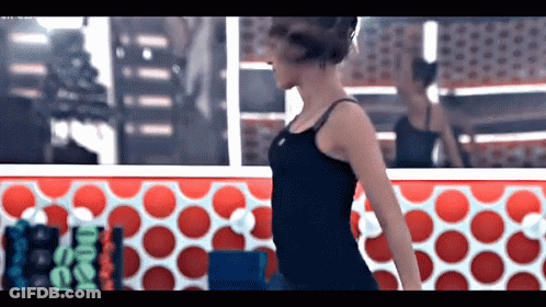 A Woman In A Black Tank Top Is Standing In Front Of A Red And White Polka Dot Wall .. GIF