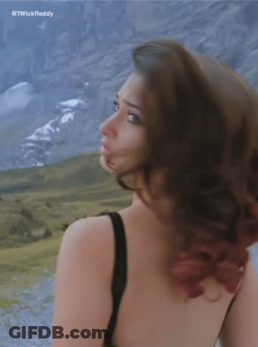 A Woman In A Black Tank Top Is Standing In Front Of Mountains GIF