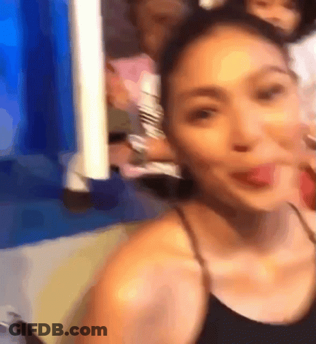 A Woman In A Black Tank Top Is Taking A Selfie With Her Tongue Out GIF