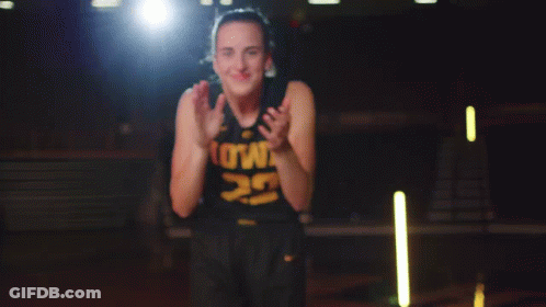 A Woman In A Black Tank Top With The Number 9 On It Is Smiling And Clapping Her Hands GIF