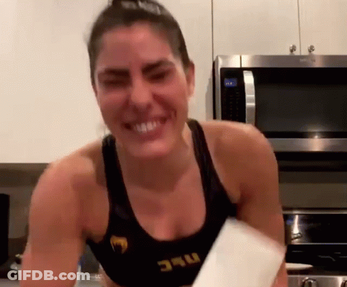 A Woman In A Black Tank Top With The Word UFC On It Is Smiling In Front Of A Microwave . GIF