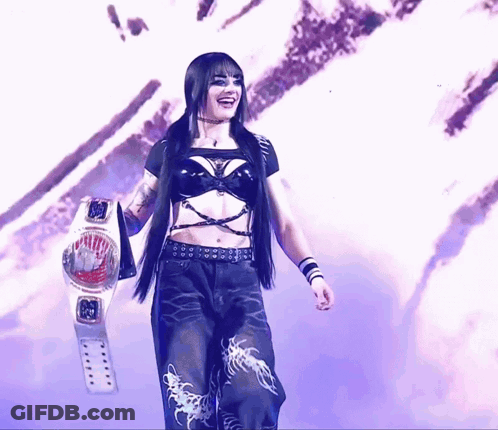 A Woman In A Black Top And Black Pants Holds A Wrestling Belt GIF