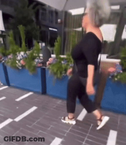 A Woman In A Black Top And Black Pants Is Walking Down The Street GIF