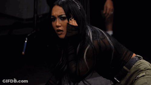 A Woman In A Black Top And Green Pants Is Kneeling Down In A Dark Room GIF