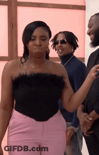 A Woman In A Black Top And Pink Pants Is Standing Next To A Man In A Blue Sweater . GIF