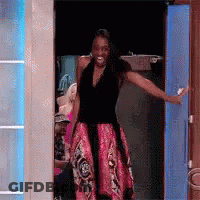 A Woman In A Black Top And Pink Skirt Is Standing In A Doorway With Her Arms Outstretched . GIF