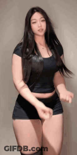 A Woman In A Black Top And Shorts Is Dancing In Front Of A Wall . GIF
