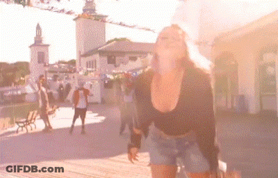 A Woman In A Black Top And Shorts Is Standing In Front Of A Crowd Of People In A Park . GIF