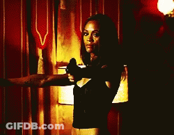 A Woman In A Black Top Is Holding A Gun GIF