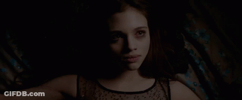 A Woman In A Black Top Is Laying Down In The Dark GIF